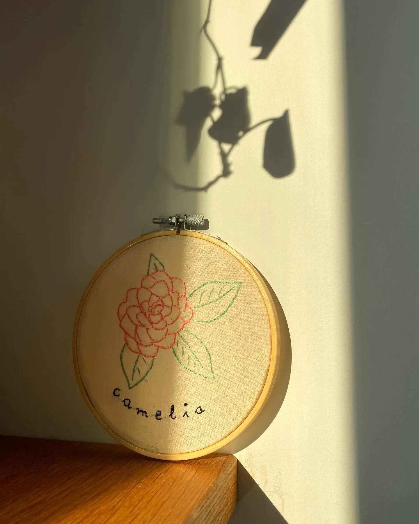 Bastidor con una camelia rosa bordada y la palabra camelia