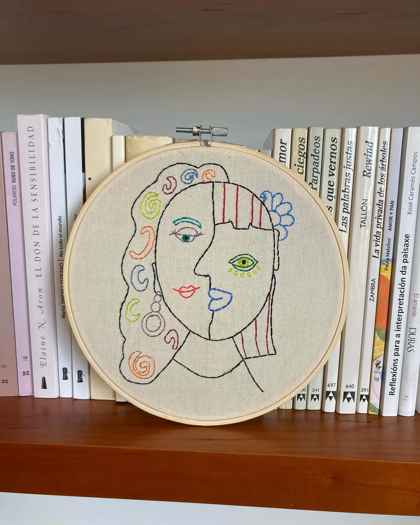 Bastidor con el rostro de una mujer bordado a línea, en una estantería de libros