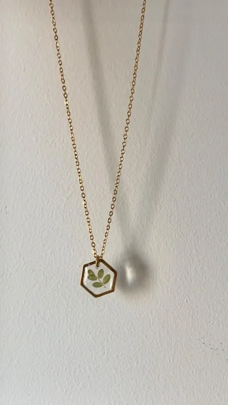 Colgante hexagonal dorado con hojas verdes colgando frente a una pared blanca