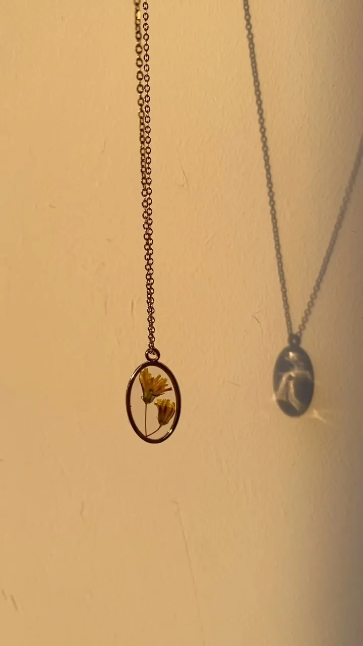 Colgante de óvalo dorado con flores amarillas colgando frente a una pared clara