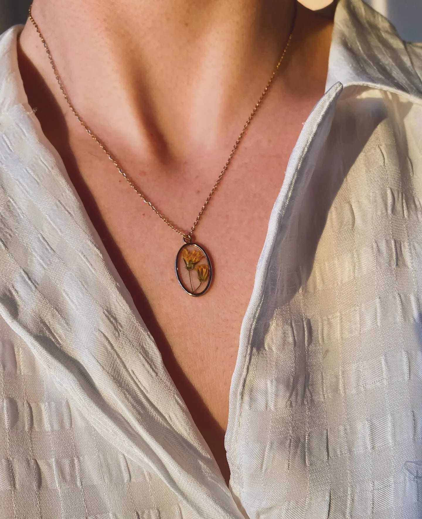 Colgante ovalado con flores naranjas puesto al cuello, con camisa blanca