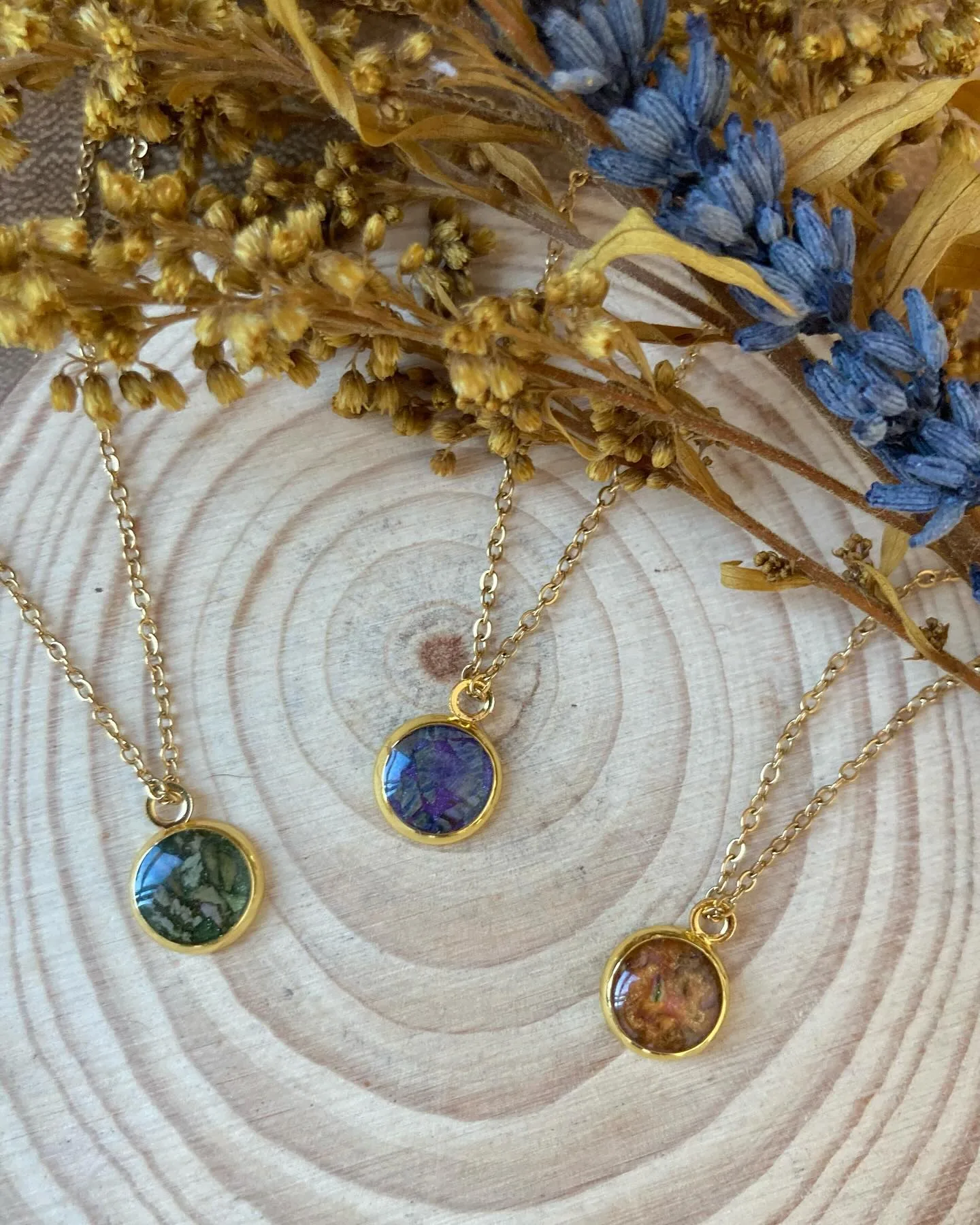 Tres colgantes redondos verde, azul y ámbar sobre una rodaja de madera con flores secas