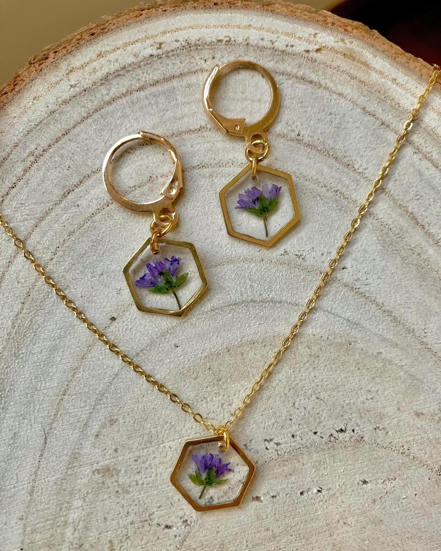Colgante y pendientes hexagonales con flores moradas sobre un plato de madera