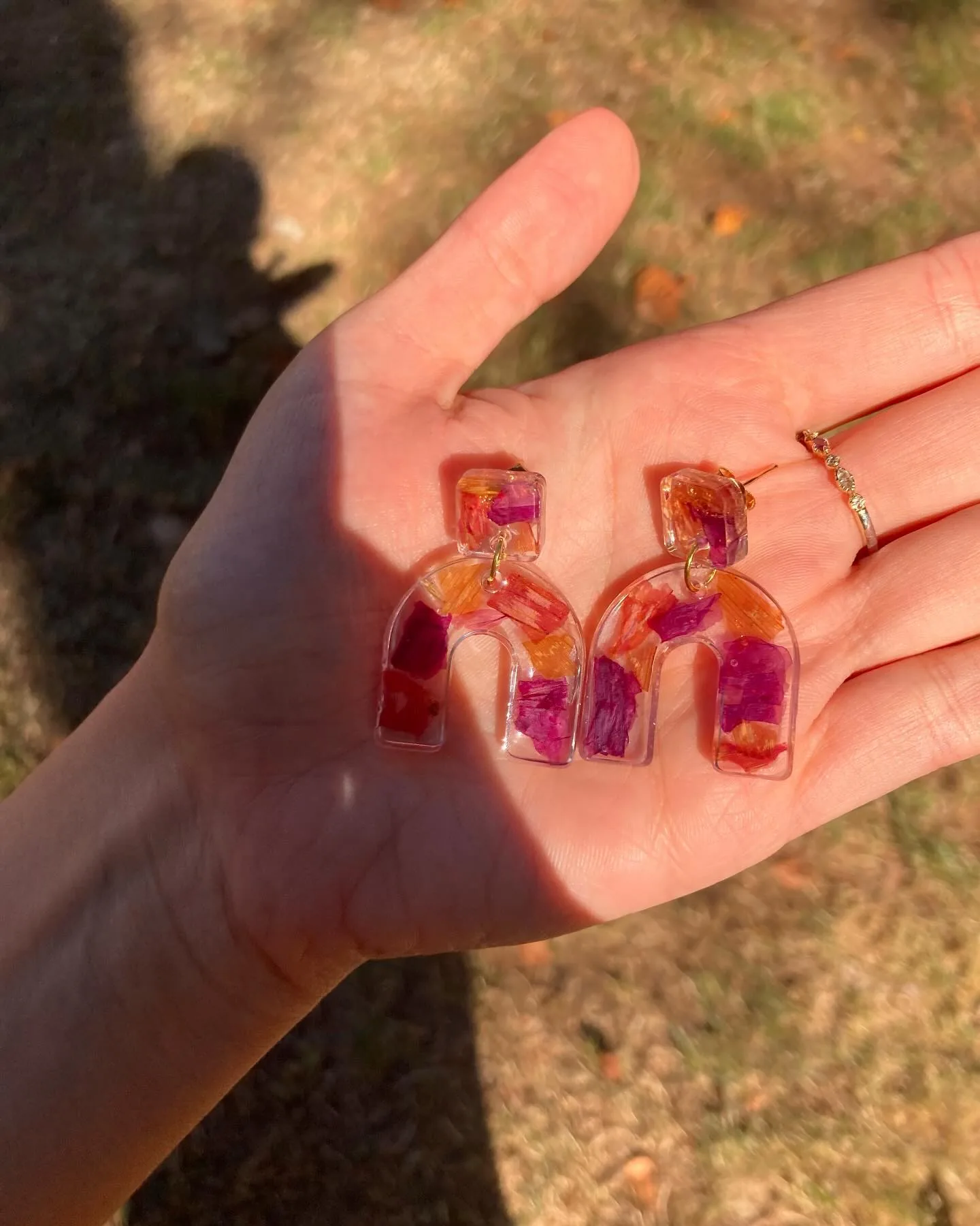 Dos pendientes de arco con pétalos fucsias y naranjas en la palma de una mano al sol