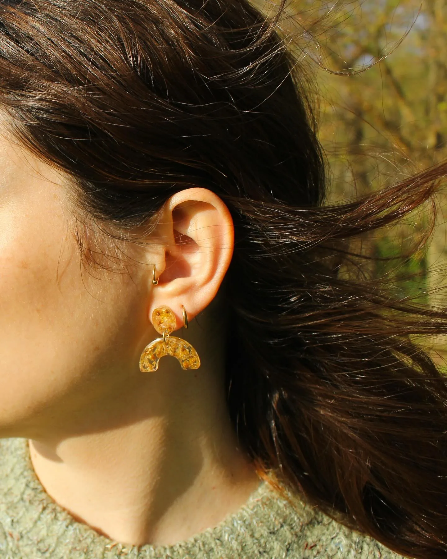 Pendiente de arco color mostaza puesto en la oreja, con el pelo al viento