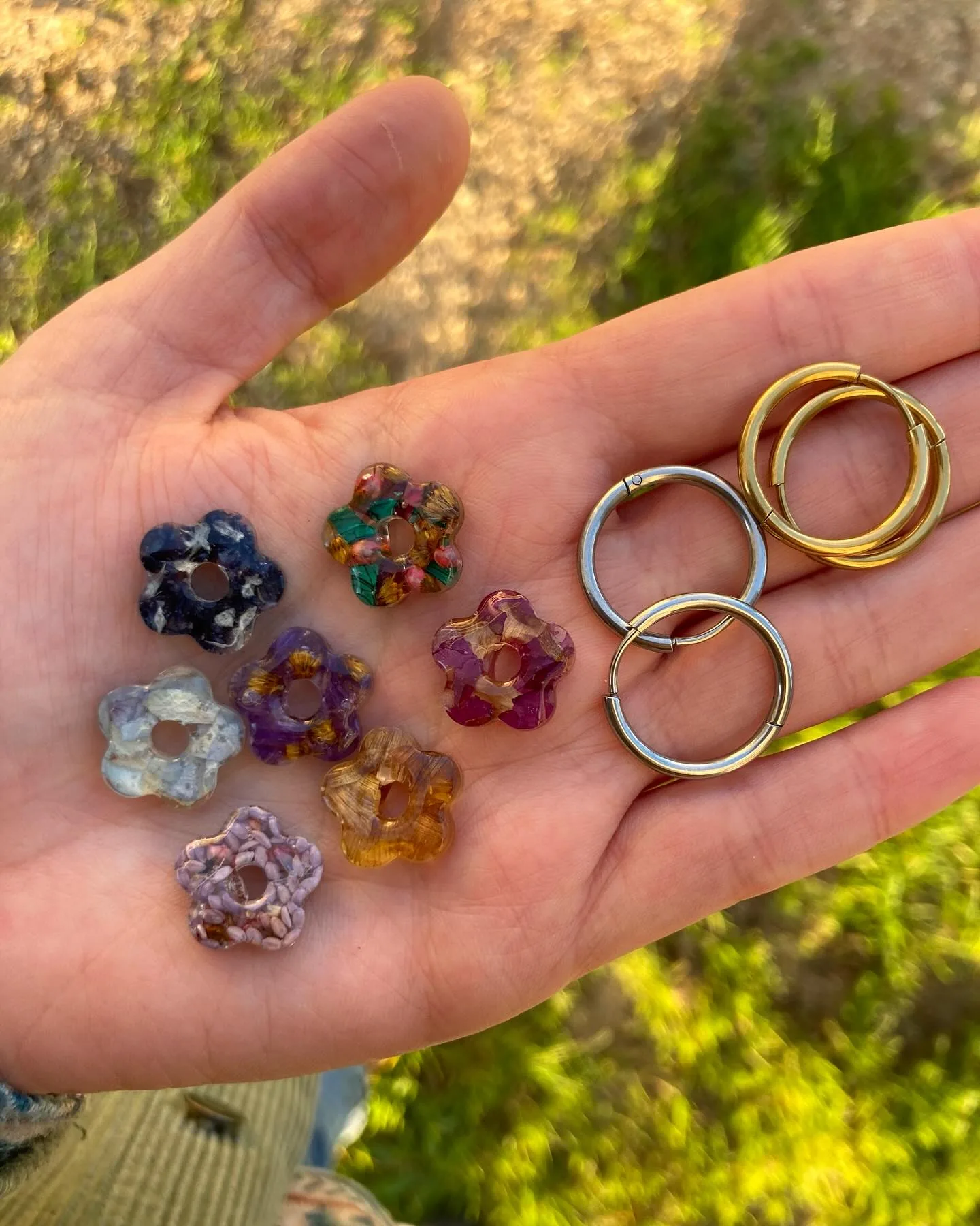 Siete flores de resina de colores y dos pares de aros en la palma de una mano
