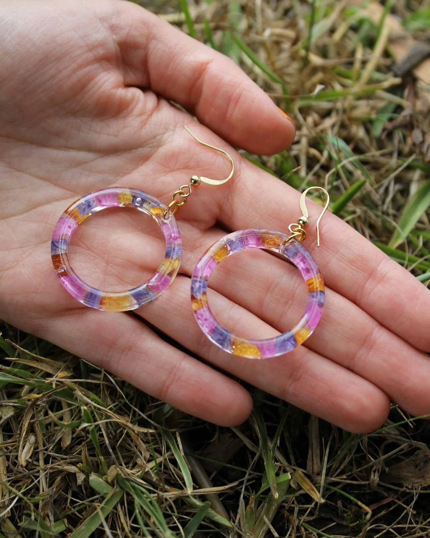 Dos aros de resina con pétalos de colores en la palma de una mano