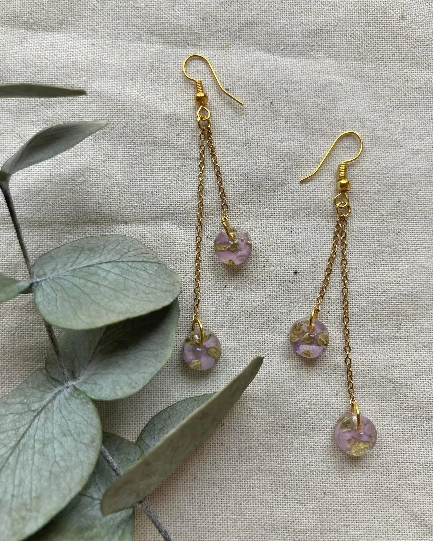 Pendientes largos de cadena con dos discos rosas, sobre lino junto a eucalipto