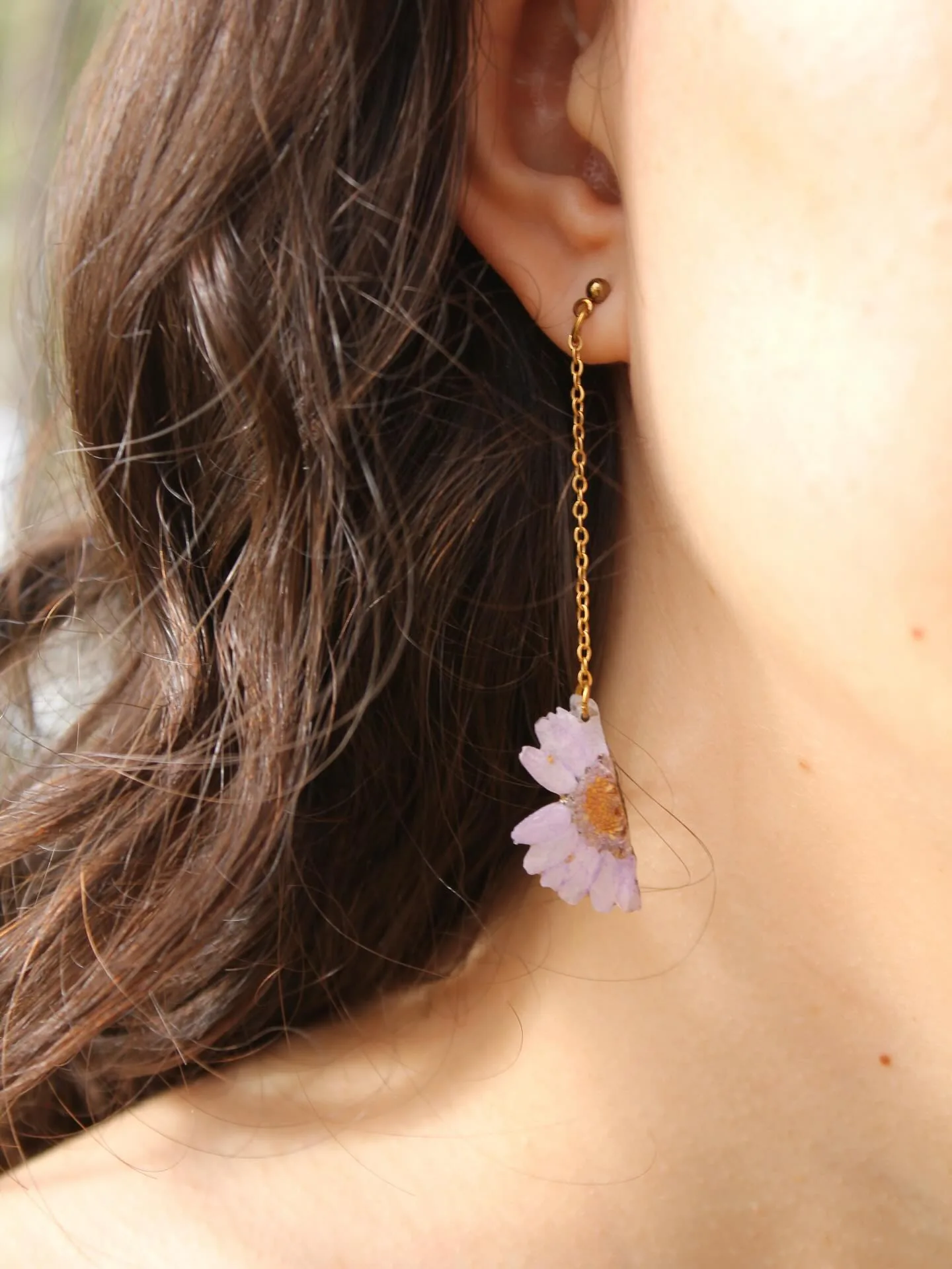 Pendiente largo con una margarita rosa en resina, junto al cuello