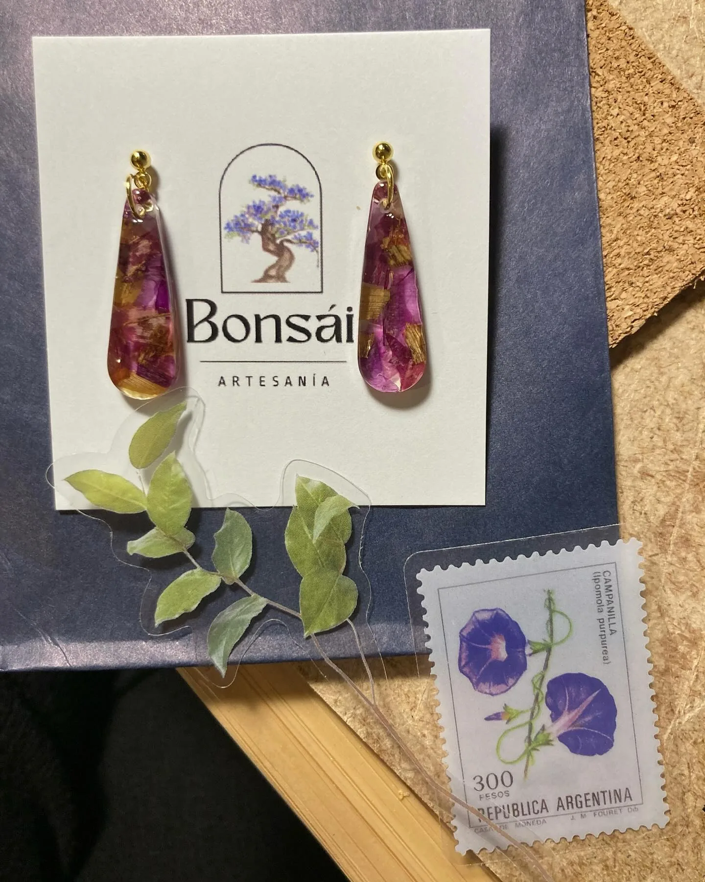 Pendientes de gota larga fucsia en su tarjeta, junto a un sello de campanilla
