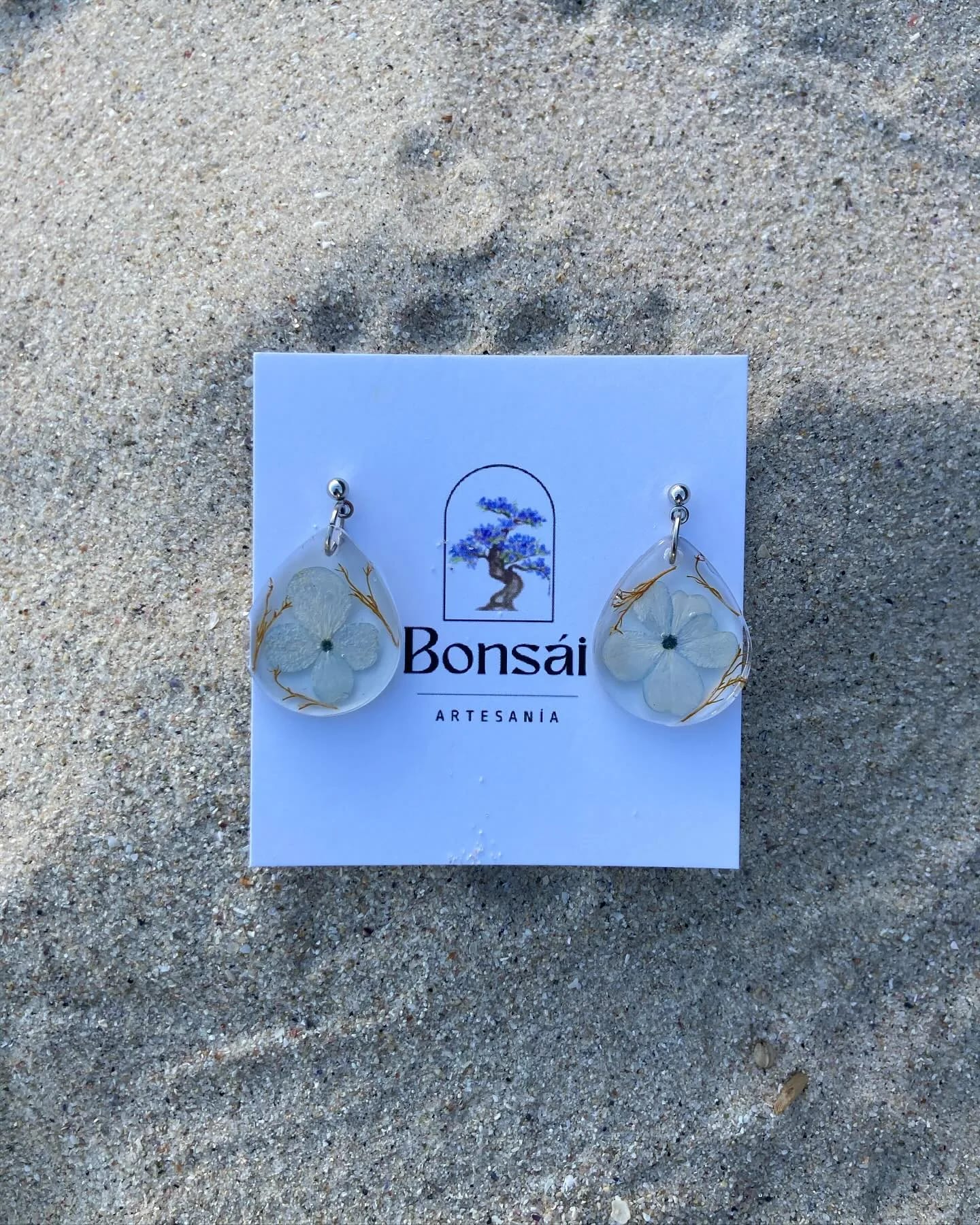 Pendientes de gota con hortensia blanca en su tarjeta, sobre la arena de la playa