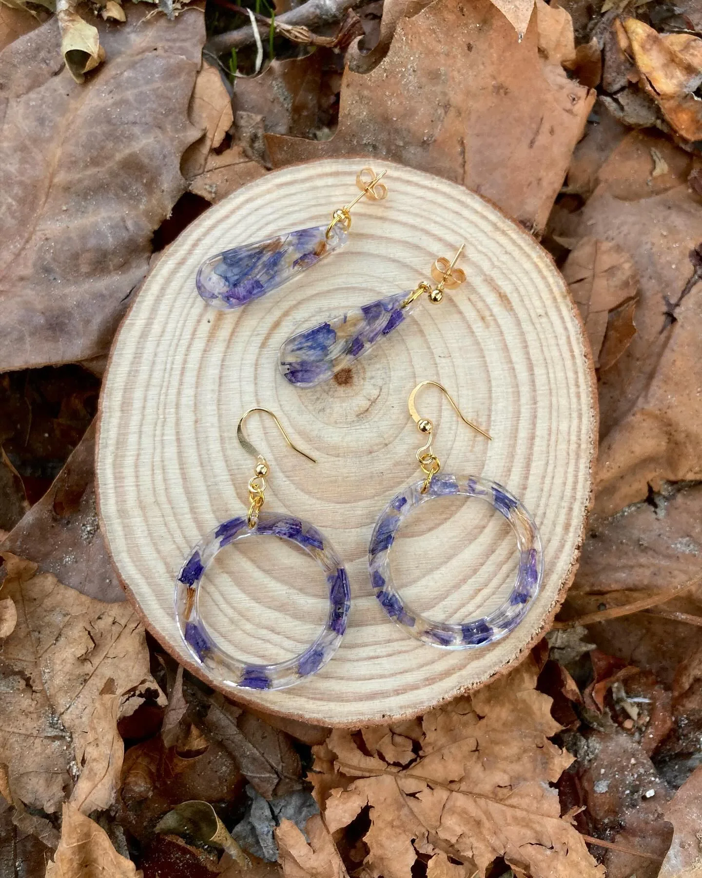 Dos pares de pendientes con lavanda sobre una rodaja de madera entre hojas secas