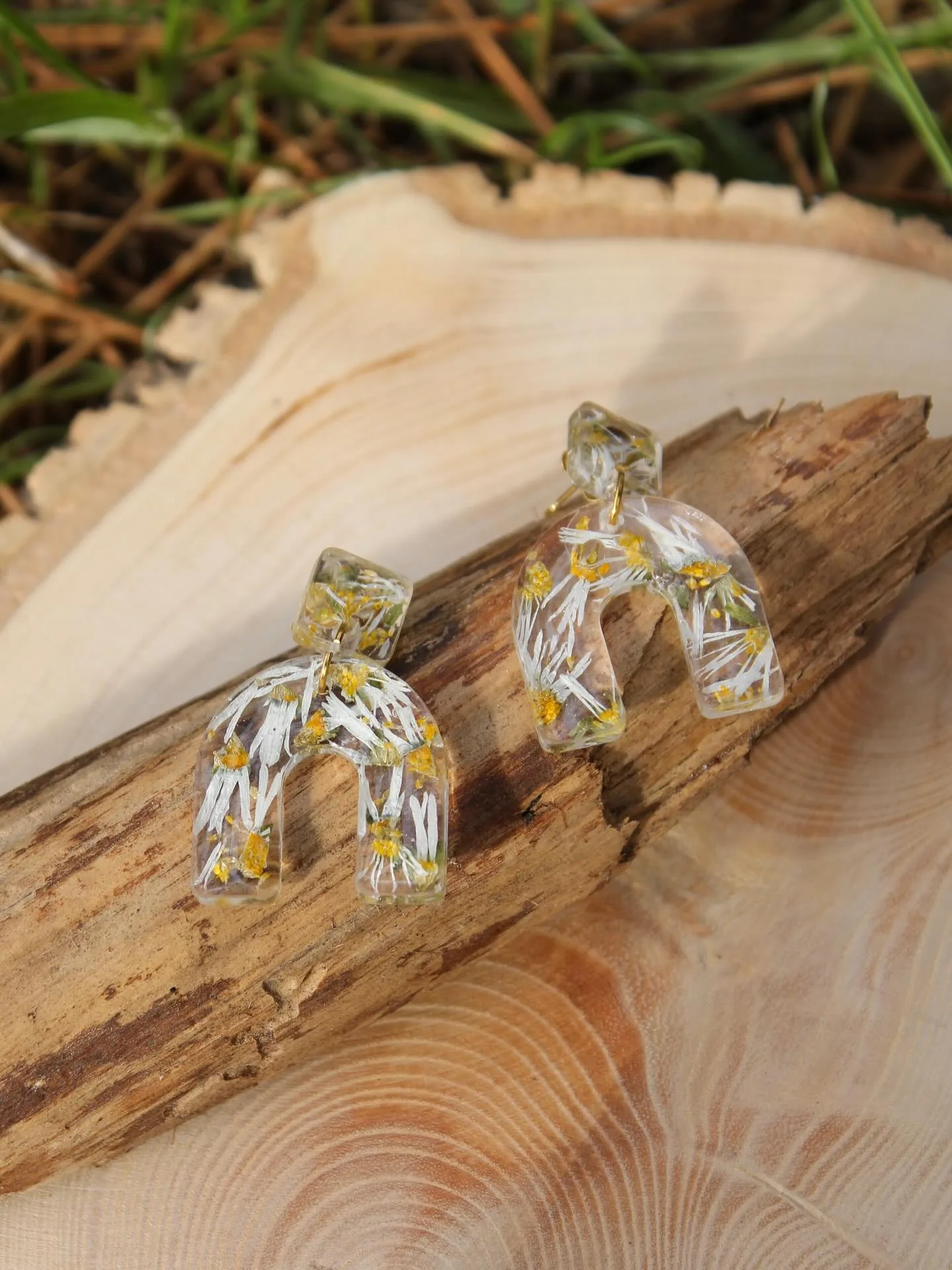 Dos pendientes de arco transparente con margaritas, sobre un tronco