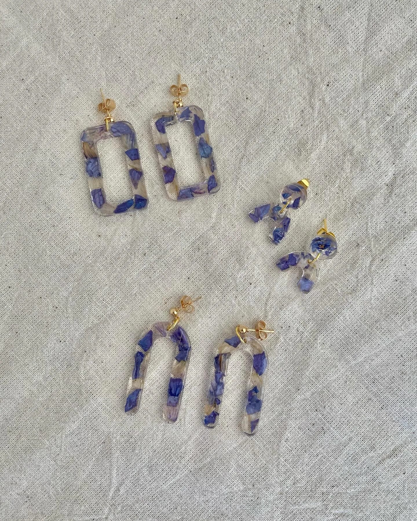 Tres pares de pendientes de resina con trozos de pétalo azul sobre tela clara