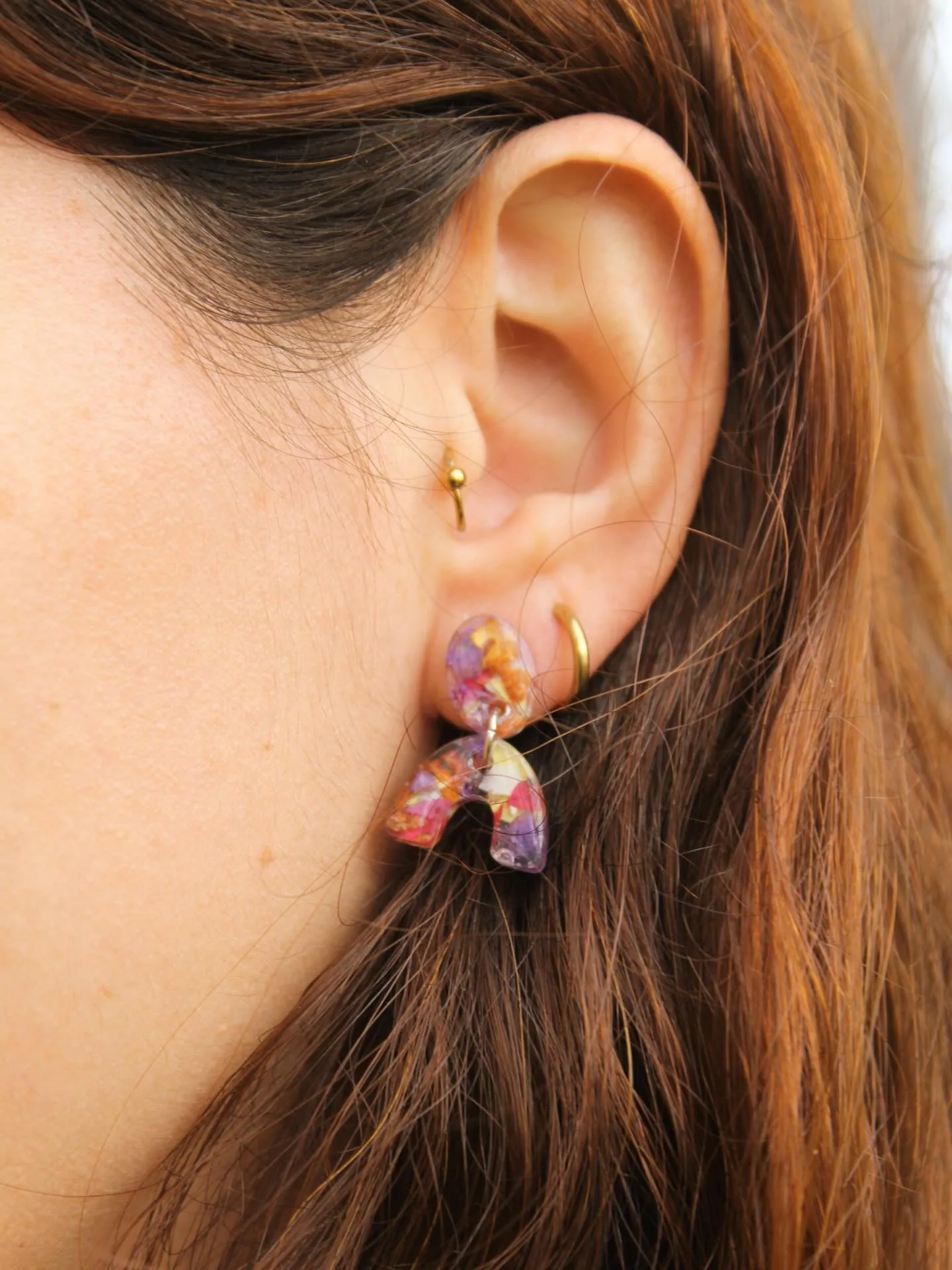 Pendientes de resina con pétalos de colores puestos en una oreja