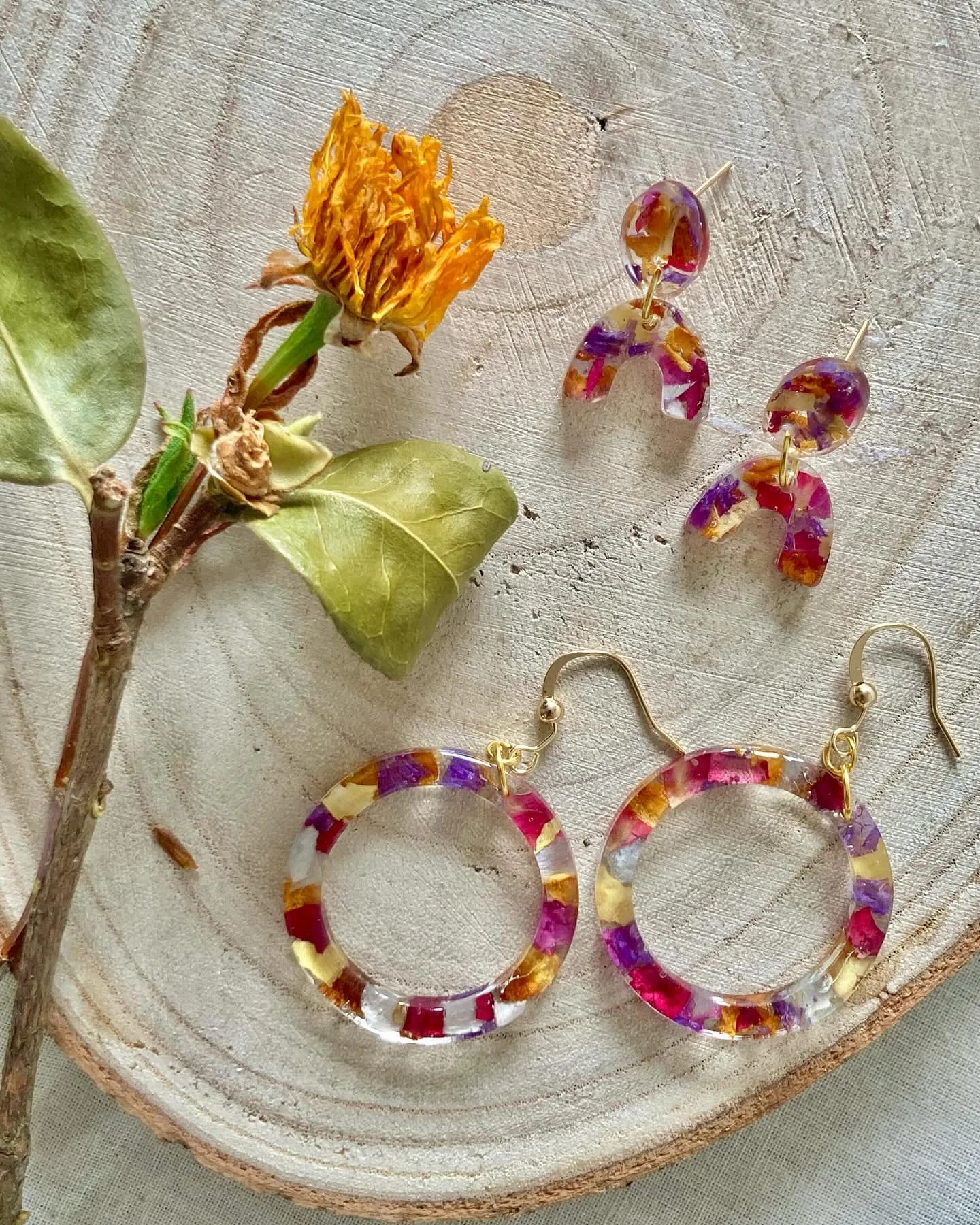 Dos pares de pendientes con pétalos de muchos colores sobre una rodaja de madera