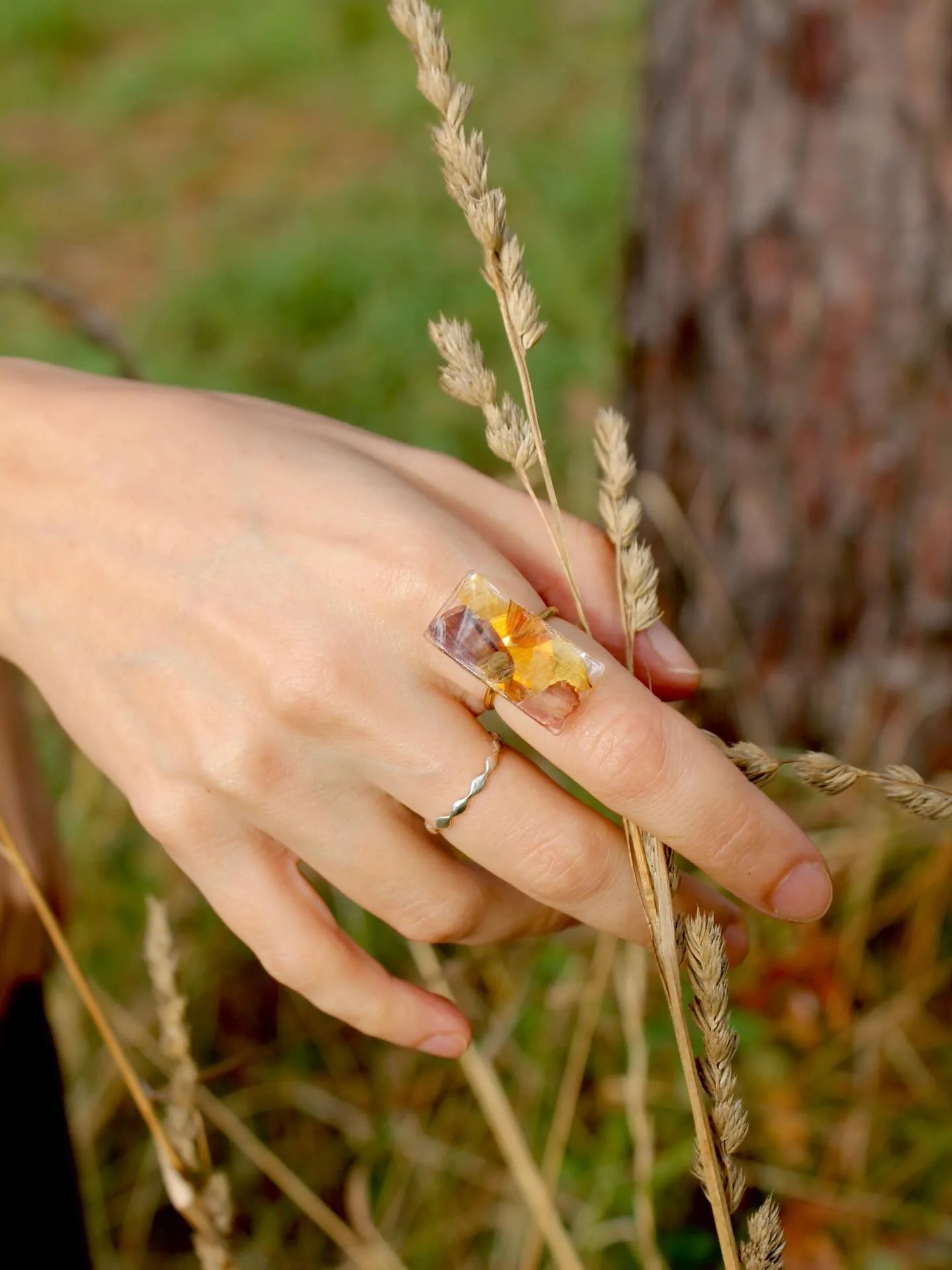 Anillo de resina con flores amarillas en una mano, entre espigas