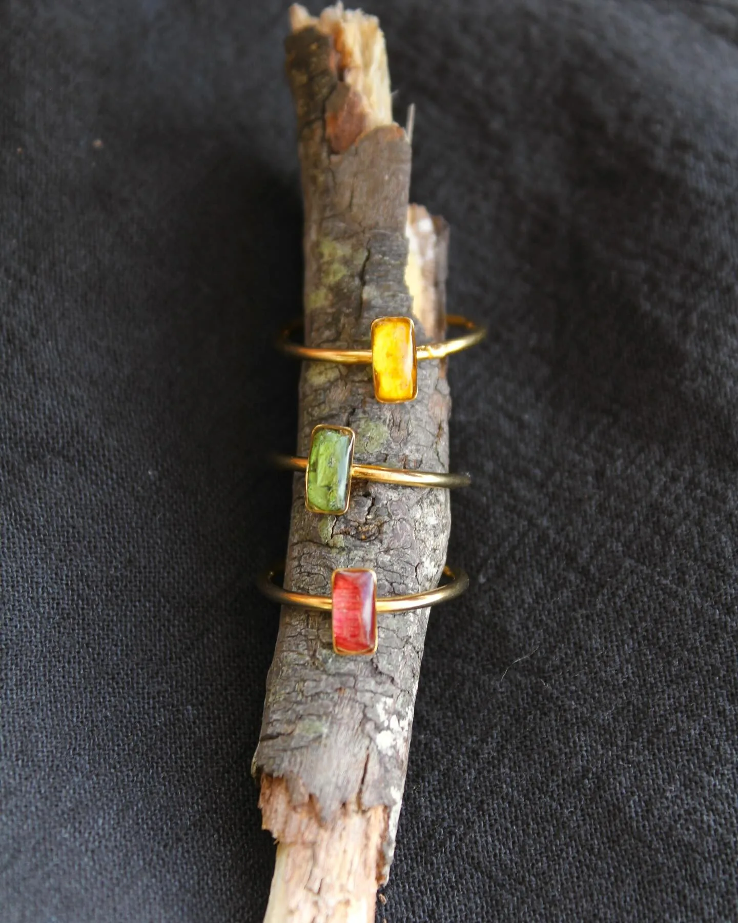 Tres anillos dorados con piedras de resina amarilla, verde y roja sobre una rama